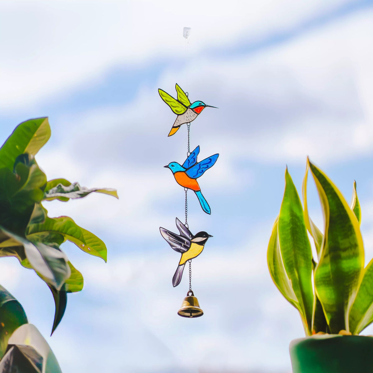 Decorative hanging with colorful stained glass bird shapes and a bell against a blue sky.