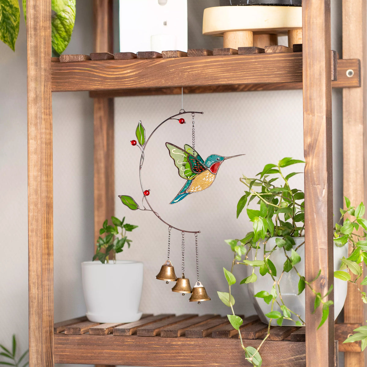 Stained glass hummingbird wind chime on a wooden shelf with plants