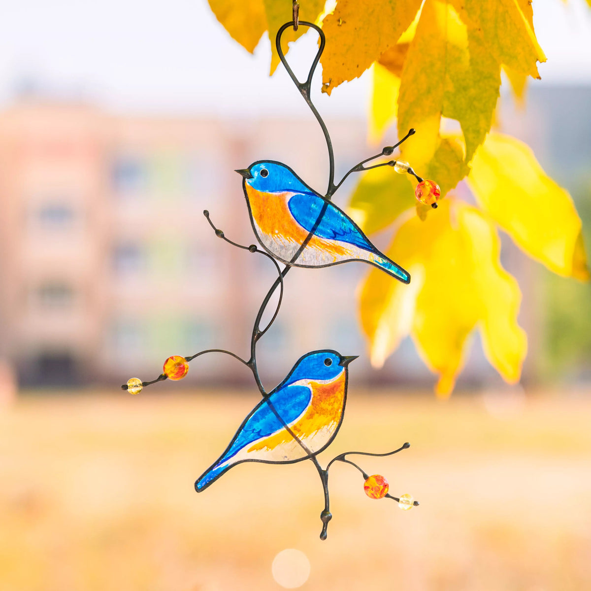 Stained glass birds on a branch with yellow leaves and blurred background
