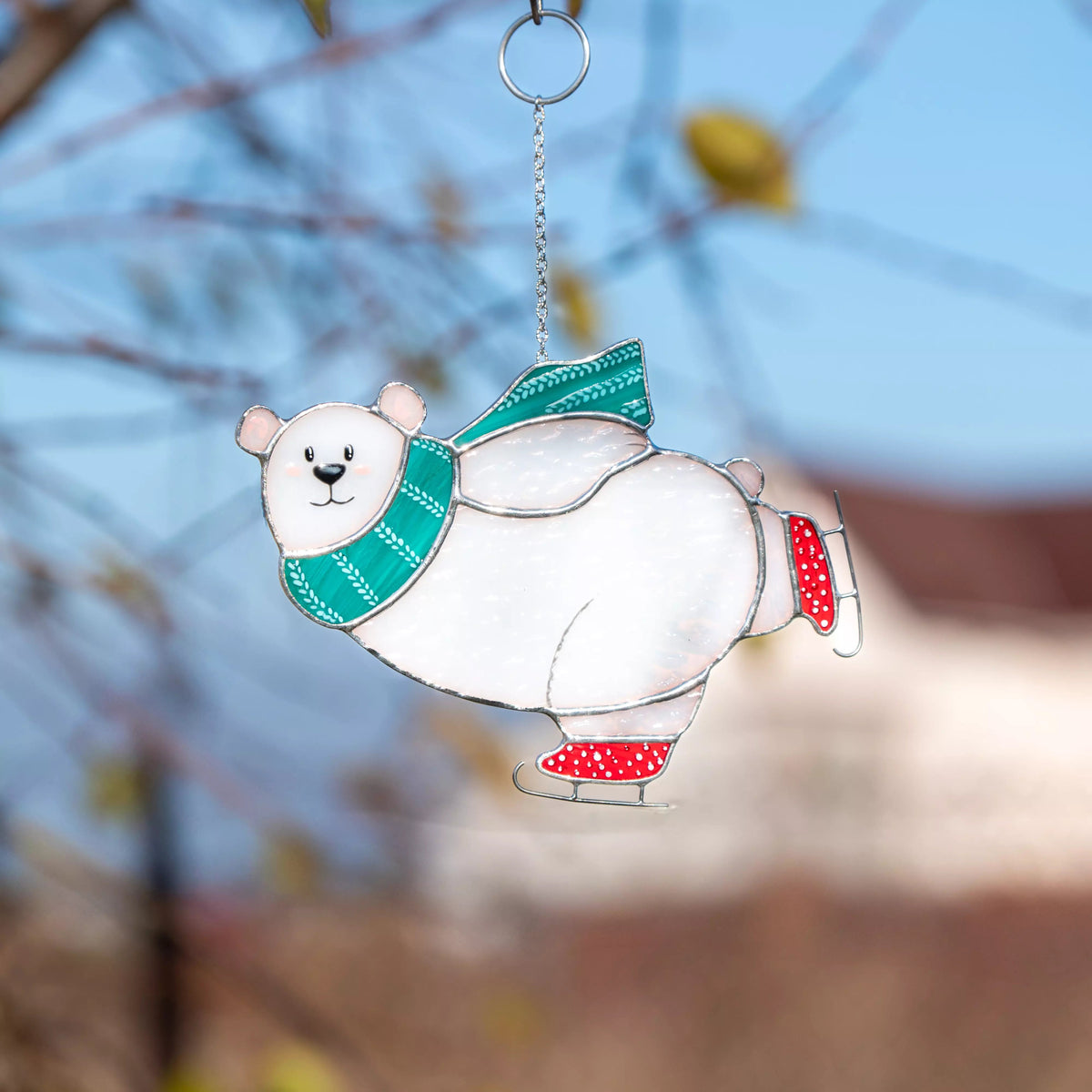 Stained glass suncatcher featuring a polar bear with a green scarf and red skates against a blurred natural background.
