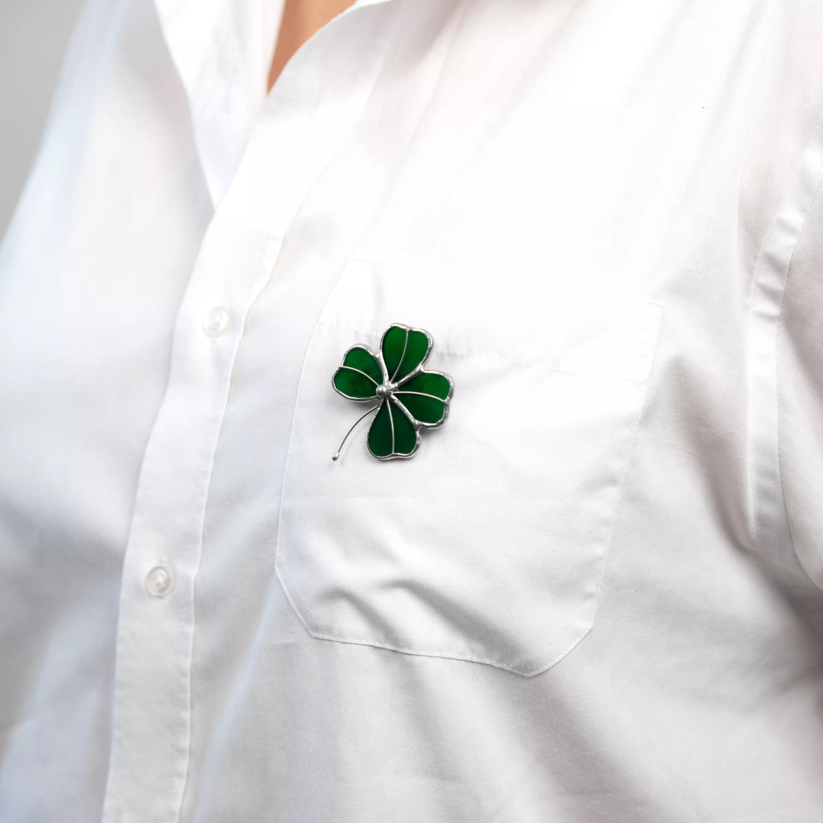 Close-up of stained glass four-leaf clover brooch pinned to chest pocket of white button-up shirt