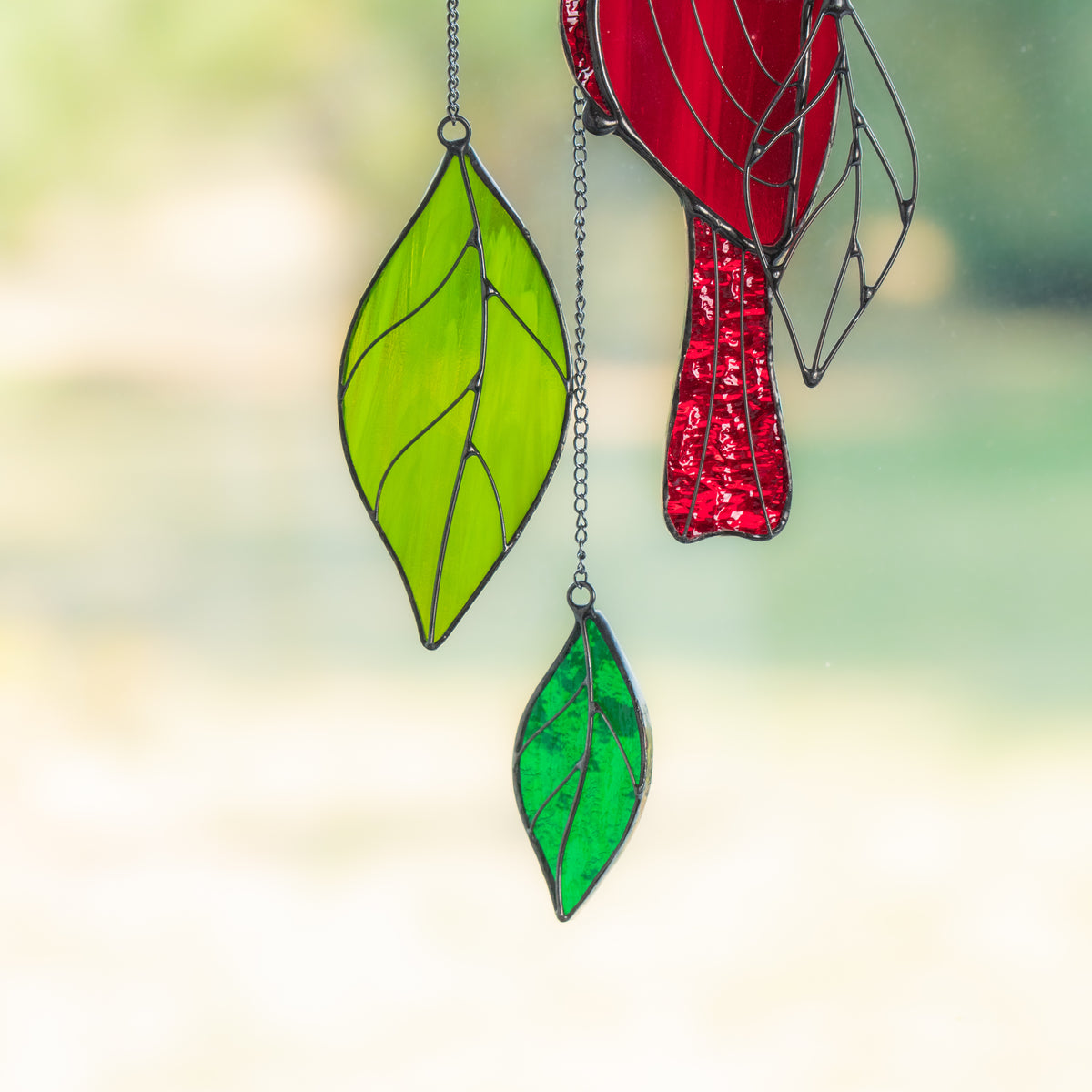 Close-up view of green stained glass leaves hanging from the cardinal suncatcher on fine metal chains.