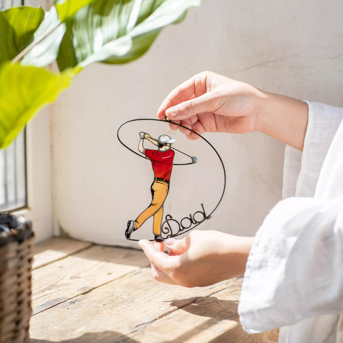 Hand holding stained glass ornament with a golfer design on a wooden surface.