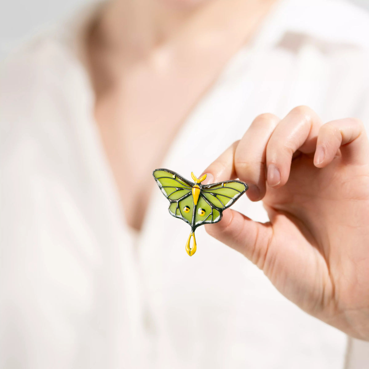 Hand holding a green butterfly stained glass luna moth pendant against a blurred background