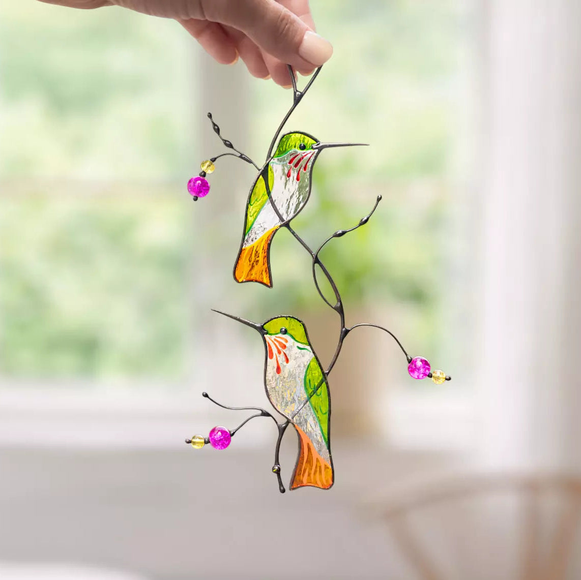 Hand holding a stained glass hummingbirds sitting on a branch suncatcher