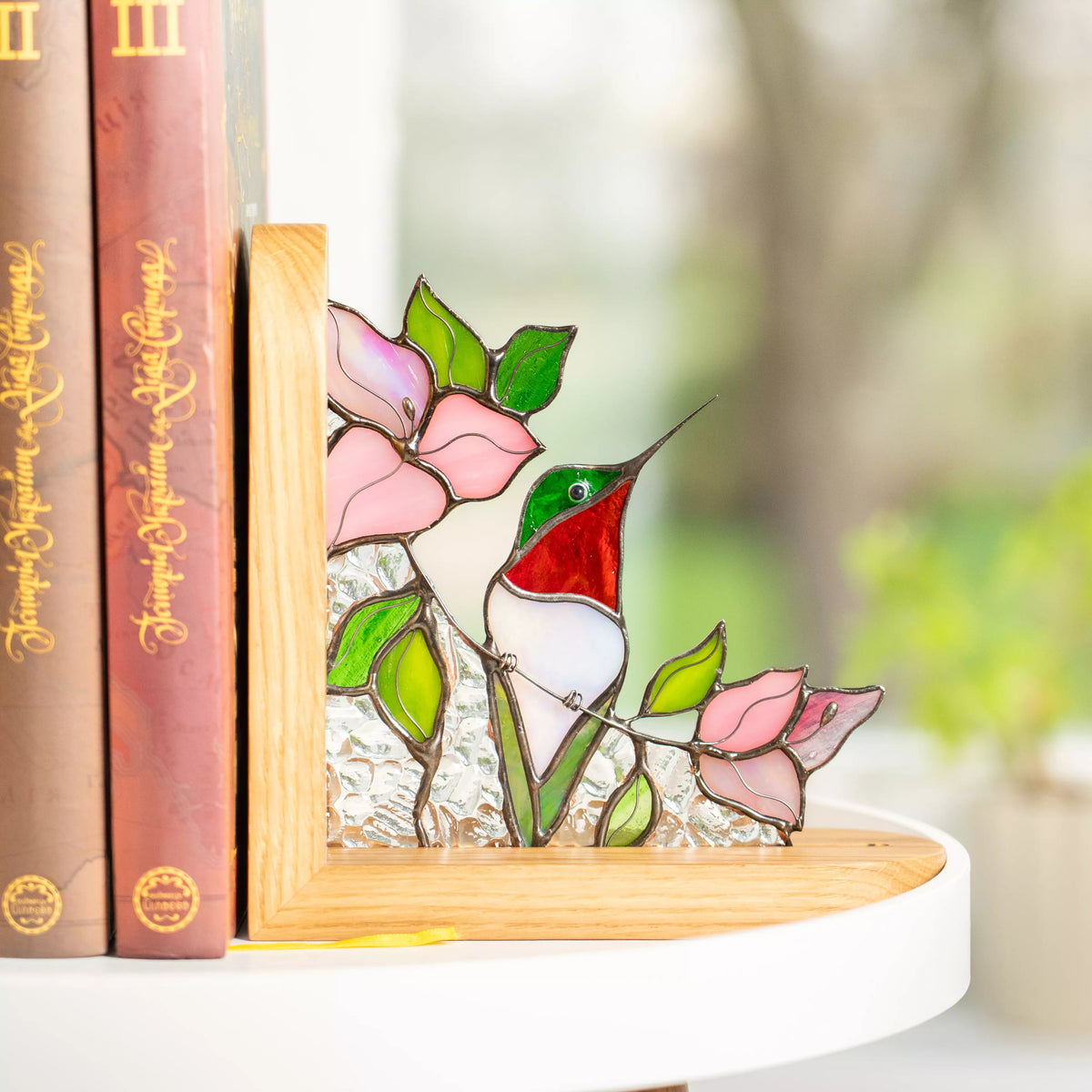 Hummingbird stained glass bookend placed next to books on a shelf with soft natural light.