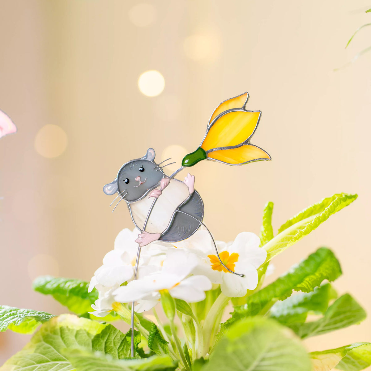 Illustration of a stained glass mouse holding a yellow flower among green leaves on a soft beige background