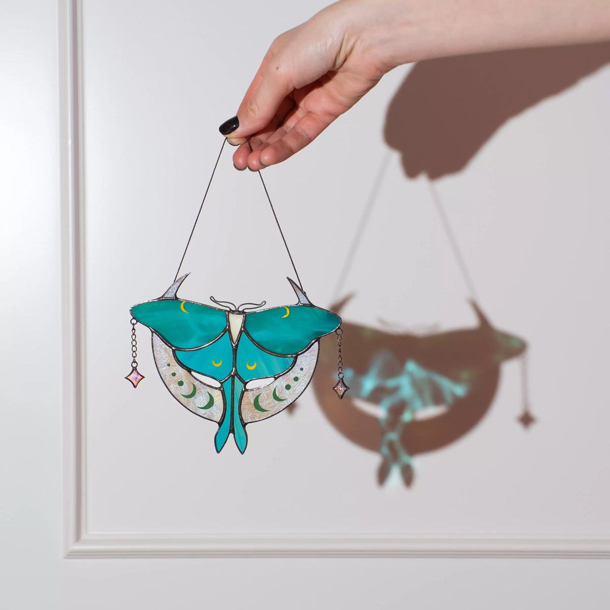 A detailed view of a Luna Moth stained glass suncatcher featuring intricate moon phases and crystals.
