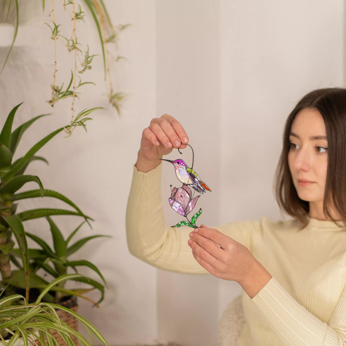 Woman holding a stained glass bird suncatcher with plants in the background