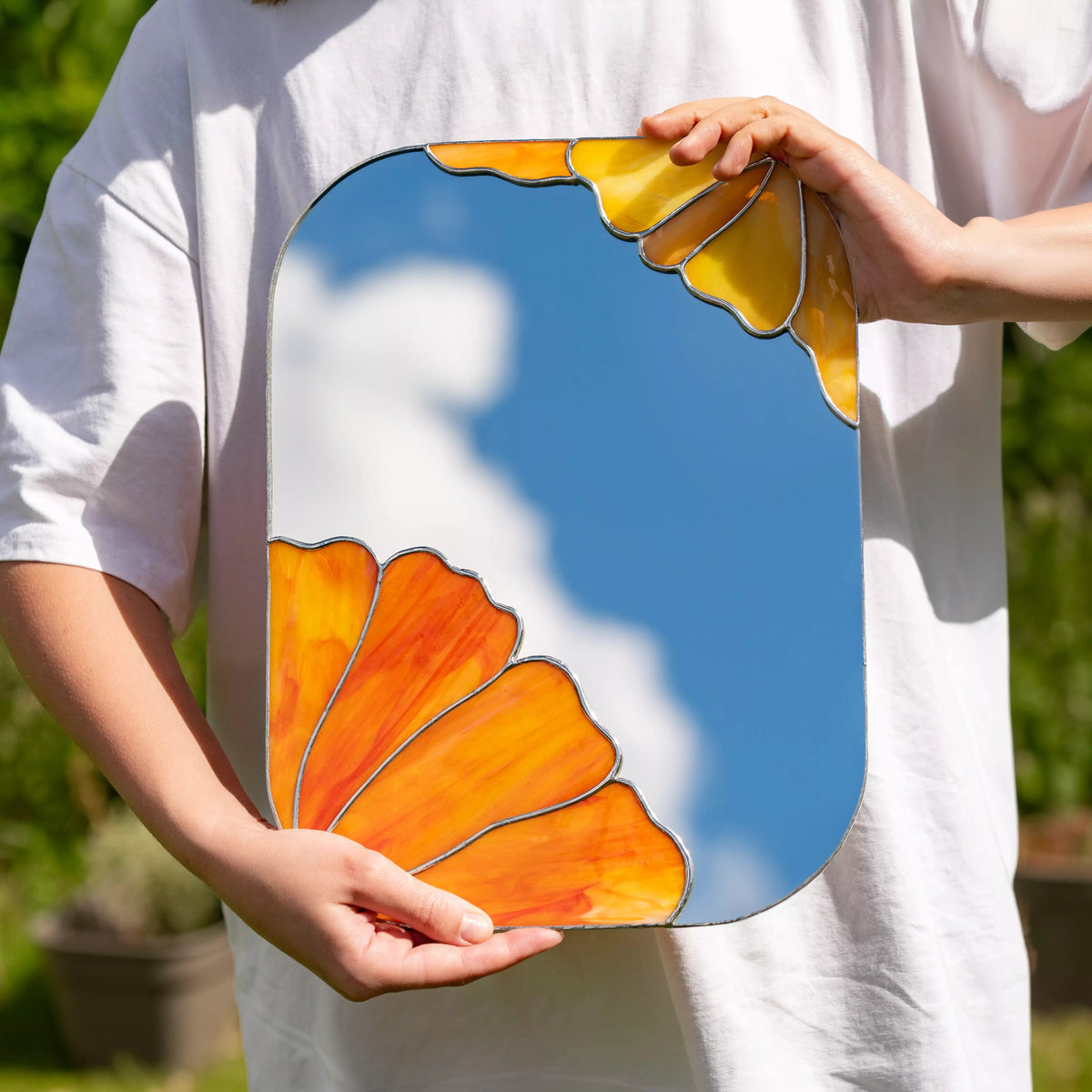 Person holding stained glass mirror with floral design outdoors