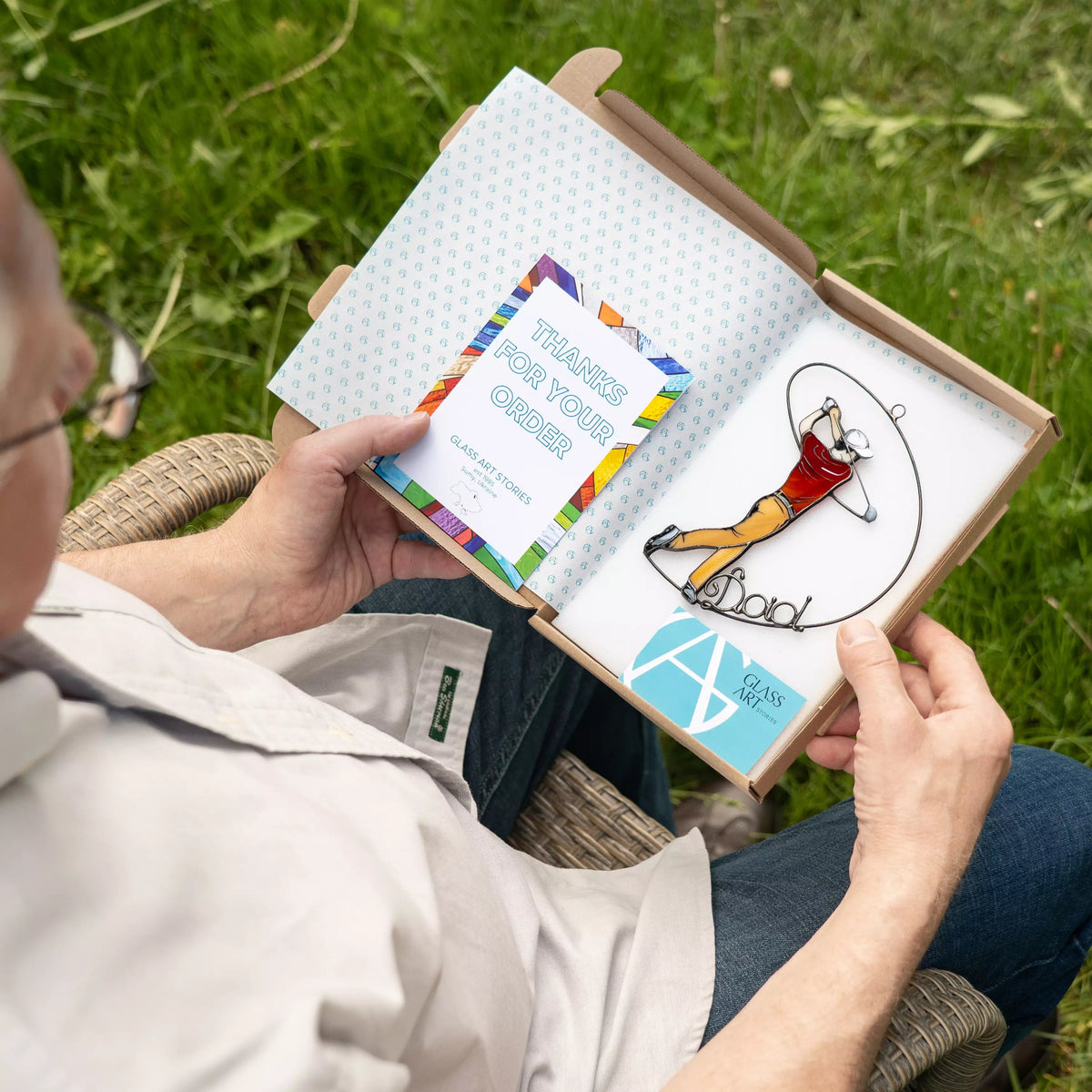 Person reading a box with stained glass suncatcher featuring golf dad on a grassy background