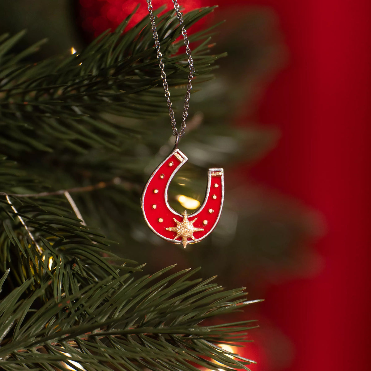 Red horseshoe stained glass necklace with a star on a Christmas tree branch.