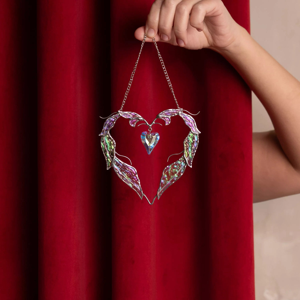 Iridescent glass feathers and a crystal heart reflect warm light, making this handmade love suncatcher a charming accent for modern home decor.