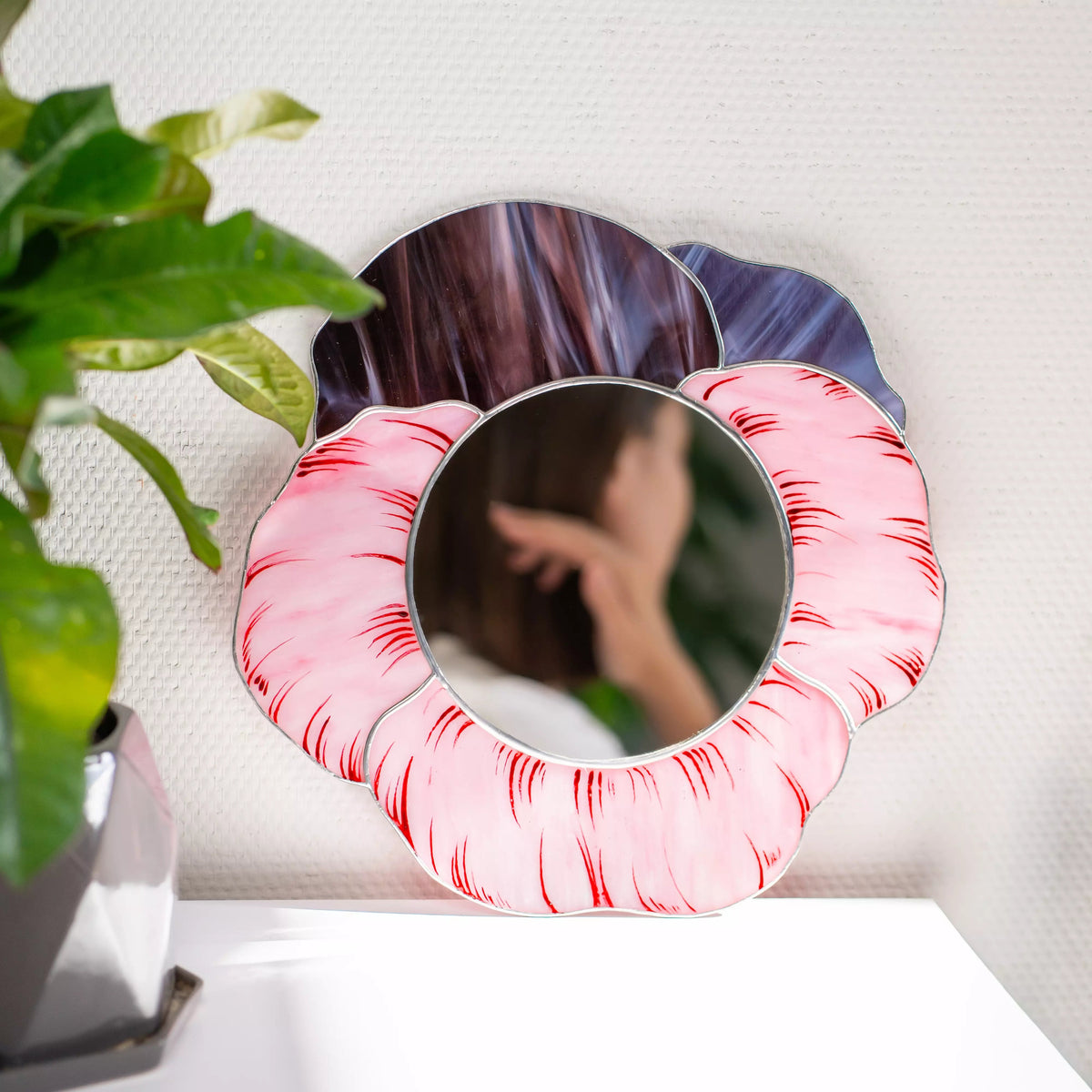 Round stained glass mirror with pink and purple abstract design on a white wall