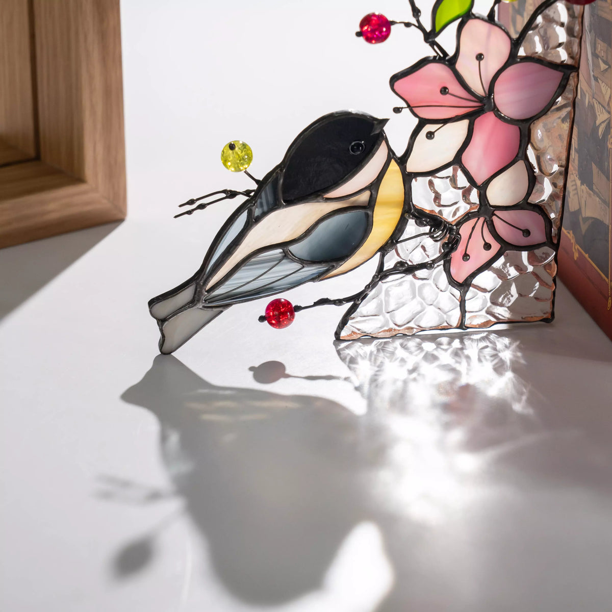 Side view of stained glass chickadee bird with layered glass feathers and bead accents, casting a soft shadow on a light surface.