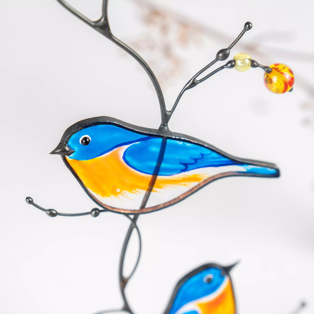 Close-up view of stained glass bird on a branch with a blurred floral background