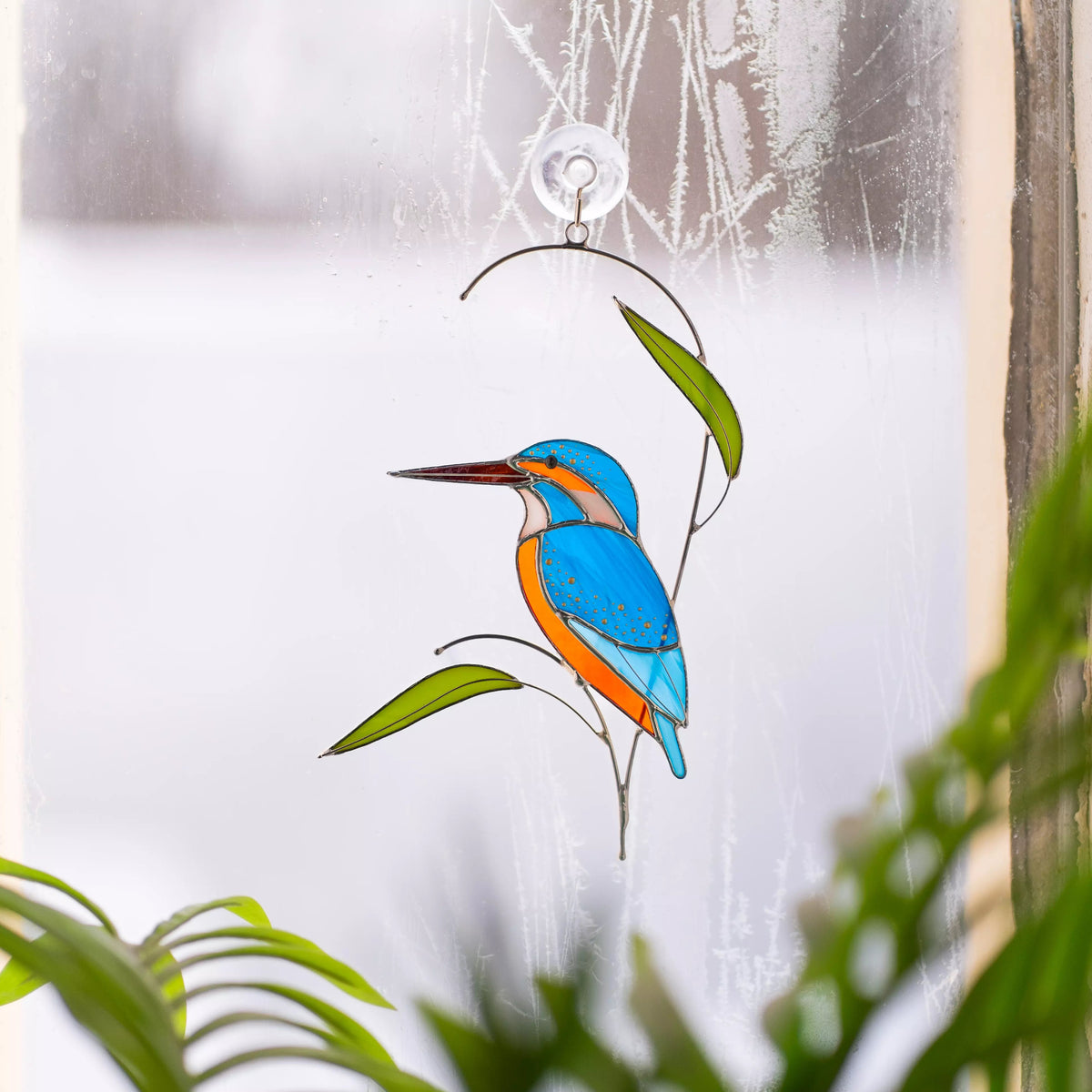 Stained glass suncatcher kingfisher hanging on a window with a blurred natural background