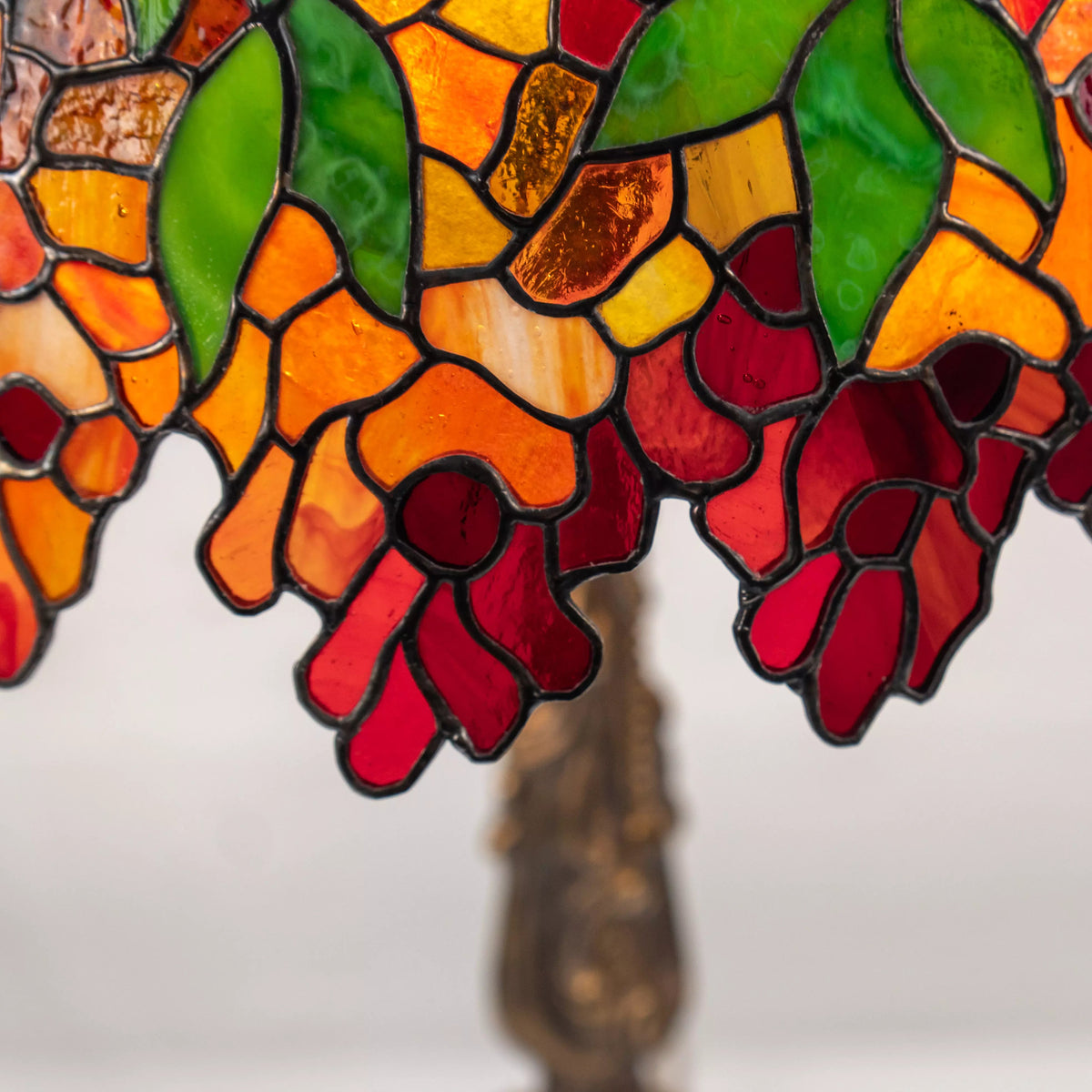 Close-up of lower part of the lamp shade with red petals, orange glass, and green leaves