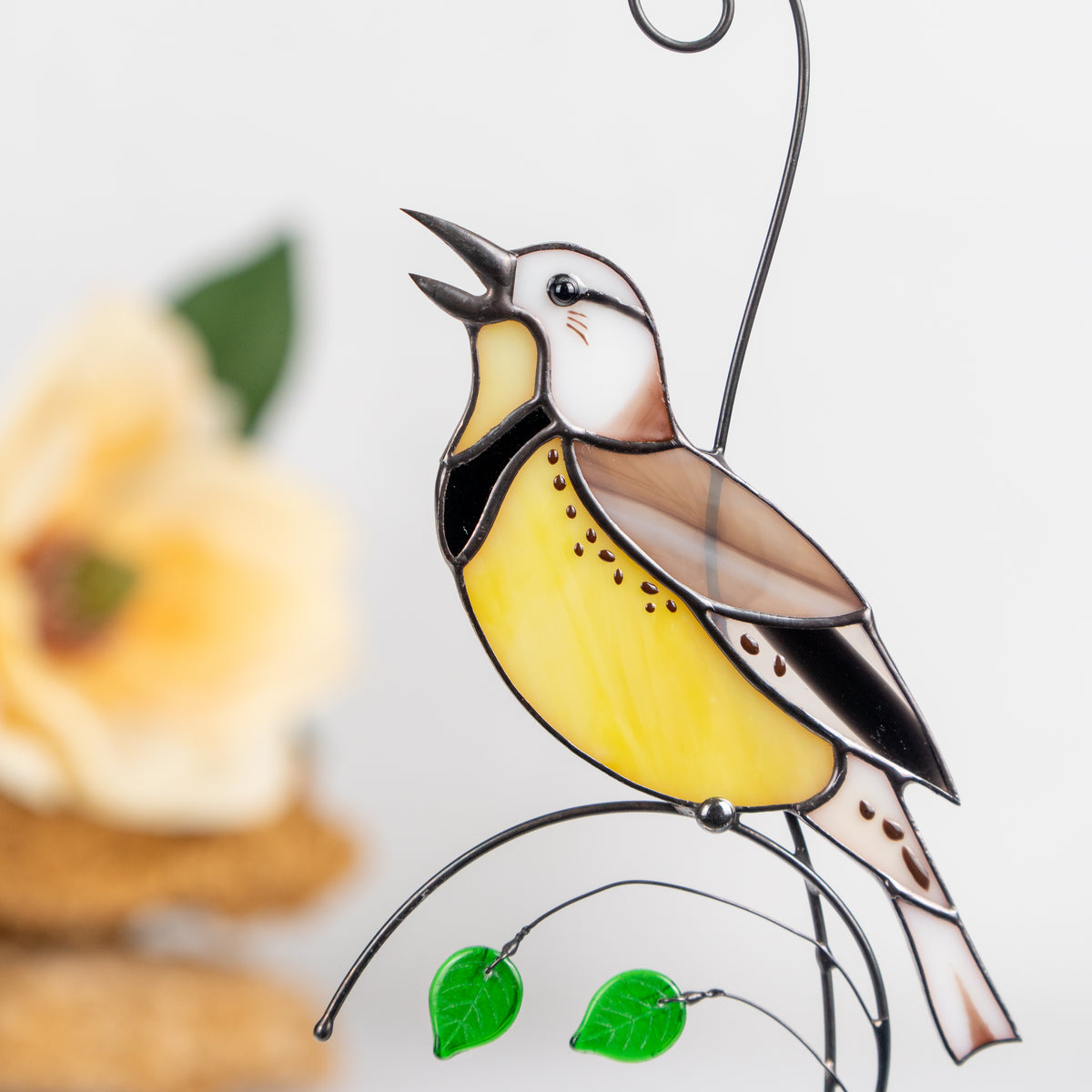 Close-up of Stained glass meadowlark suncatcher in yellow and brown, hanging with two green leaf beads.