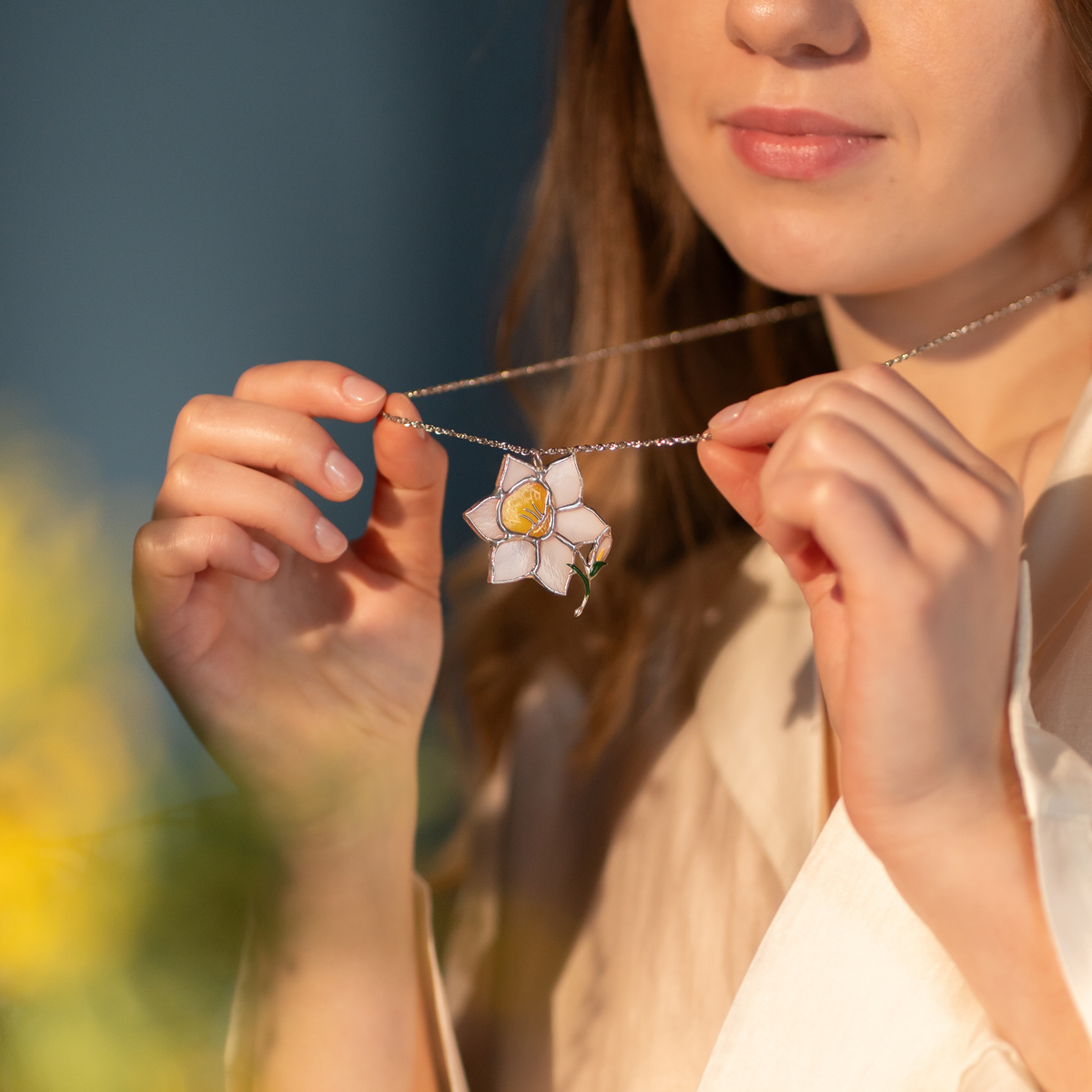 Stained glass daffodil necklace hanging on the neck with a blurred natural background 