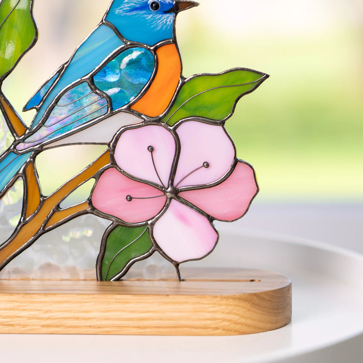 Macro view of a pink stained glass flower with green leaves beneath a blue bird.