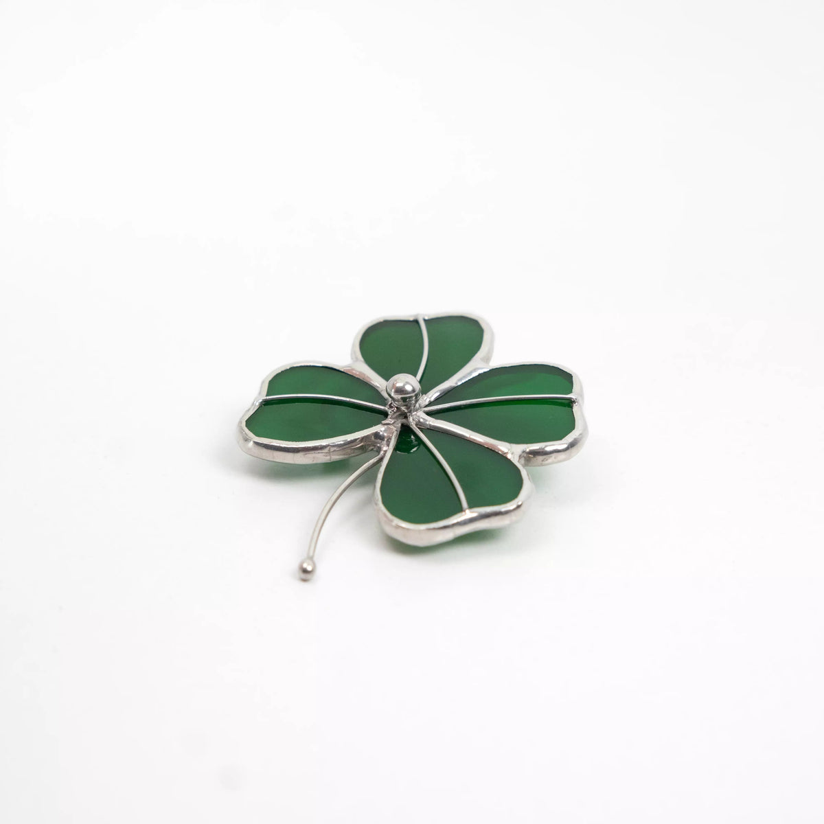 Green stained glass four-leaf clover brooch lying flat on white background
