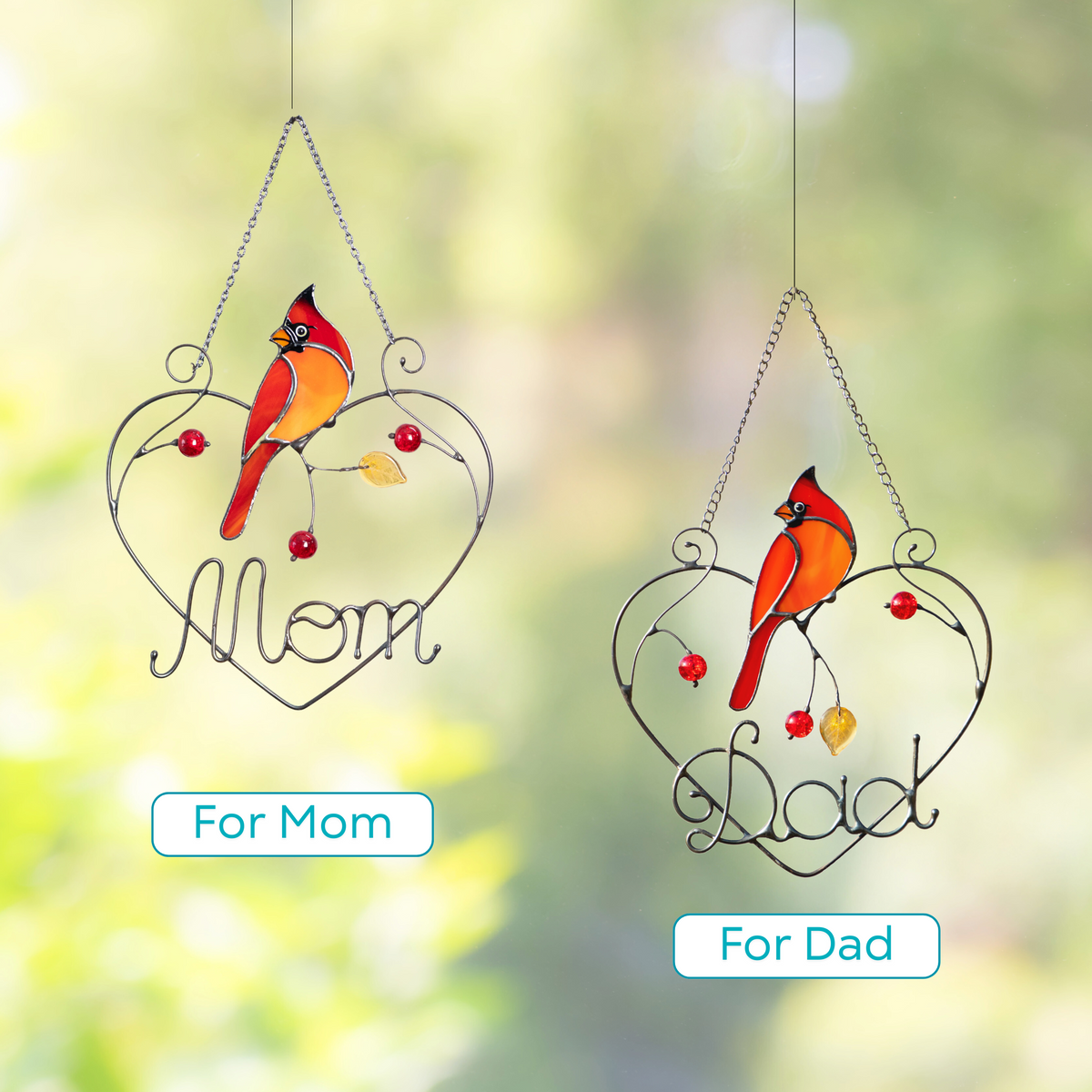 Two cardinal bird suncatchers with words “Mom” and “Dad” in metal hearts, shown outdoors.