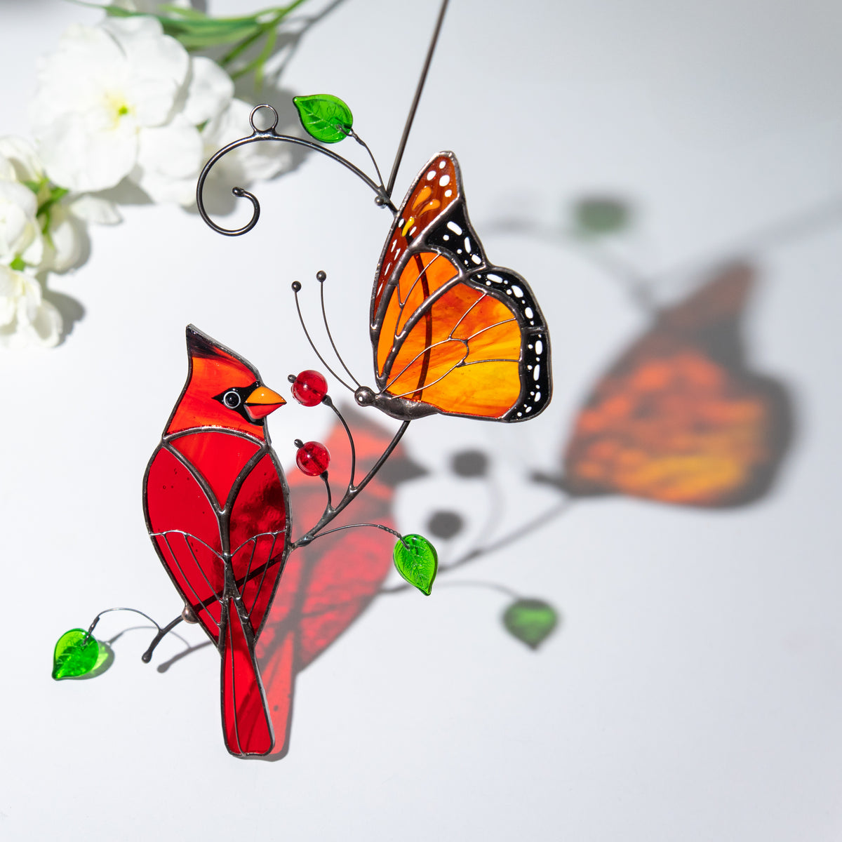 Artistic shadow play of a stained glass cardinal and monarch butterfly suncatcher with reflected colors.

