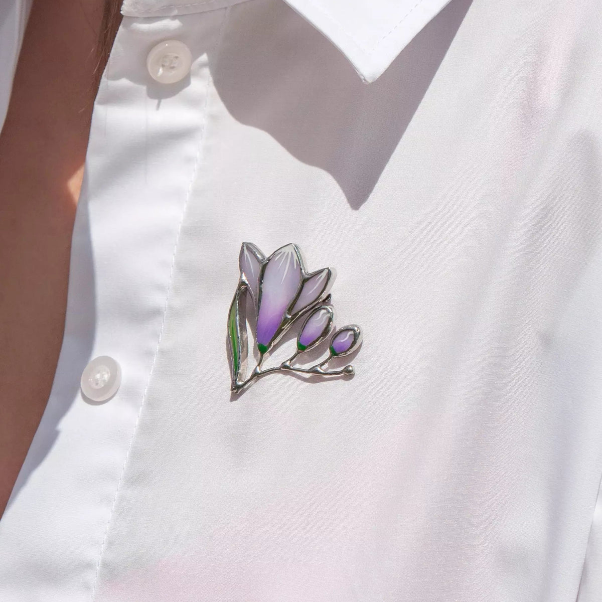 Woman wearing a white blouse with a purple freesia-shaped stained glass brooch on the chest