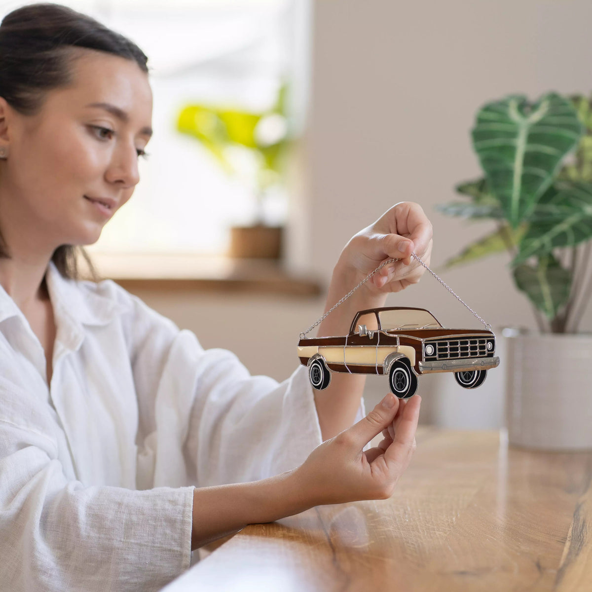 Woman holding a stained glass model of a vintage truck indoors with plants in the background
