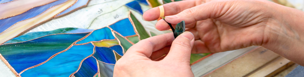 A close-up of hands holding a piece of stained glass 