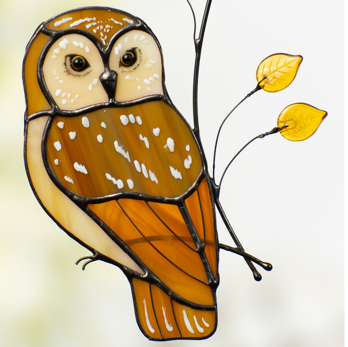 Detailed close-up of owl’s face and body, showing yellow glass leaves and stained glass textures.